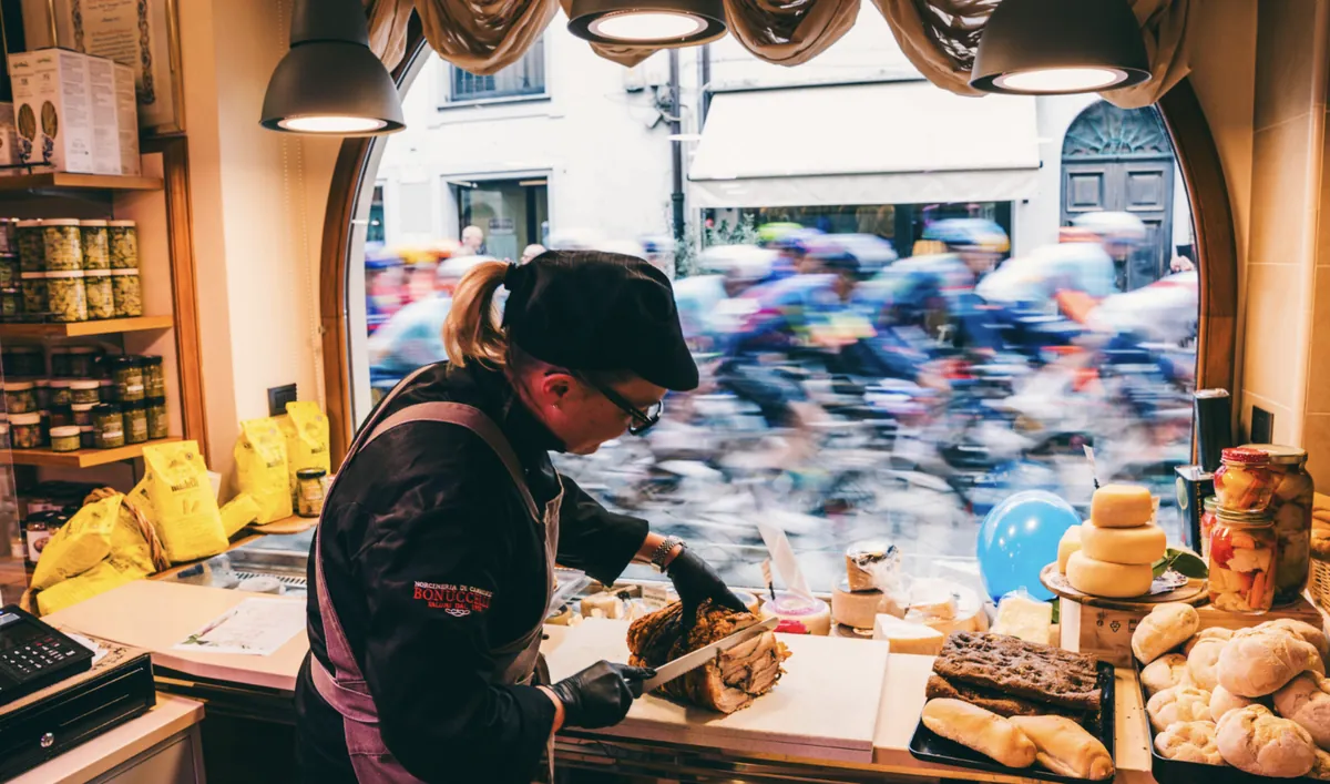 A baker at work while the peloton races past the shop window